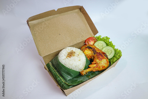 Grilled chicken served with rice, chili paste, slice of cucumber and lettuce leaves. Nasi ayam bakar lalapan, authentic recipe of Indonesian grilled chicken.
