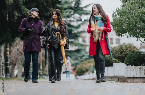 Принти на полотні A trio of fashionable women walking together on a city sidewalk during a drizzly day, enjoying their time outdoors while chatting