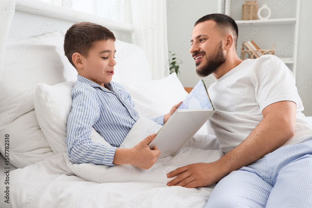 Obraz premium Happy father with his son in pajamas reading book on bed at home