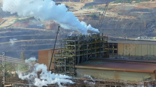 Barrick Gold mining facility with metal structures release large plumes of steam near terraced open pit mine in Cotuí, Dominican Republic. Aerial view photo