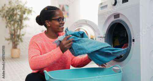 Calm woman sits on the floor, opens the washing machine door, grabs freshly washed garments, and neatly places them into a bowl beside her.