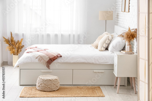 Interior of light room with big bed, table and pampas grass in vases