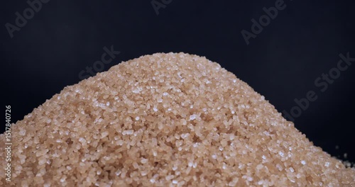 Brown cane sugar poured into pile on black background. Excessive sugar content in various products. Nutrition. The benefits or the danger of sugar consumption to health concept