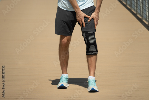 Man putting knee brace to support painful leg. Athlete bodybuilder leg wearing knee support brace or elastic kneecap bandage. Sleeve for compression. Health problems and pain.