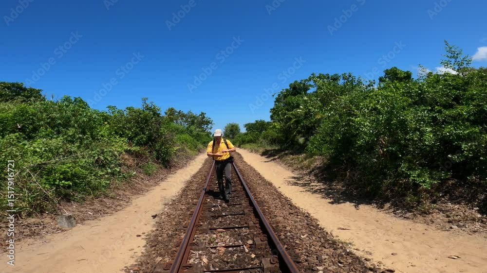 A male hiker in yellow shirt walks along a railway track running between the Canal des Pangalanes and the east coast of Madagascar, A man walking towards camera