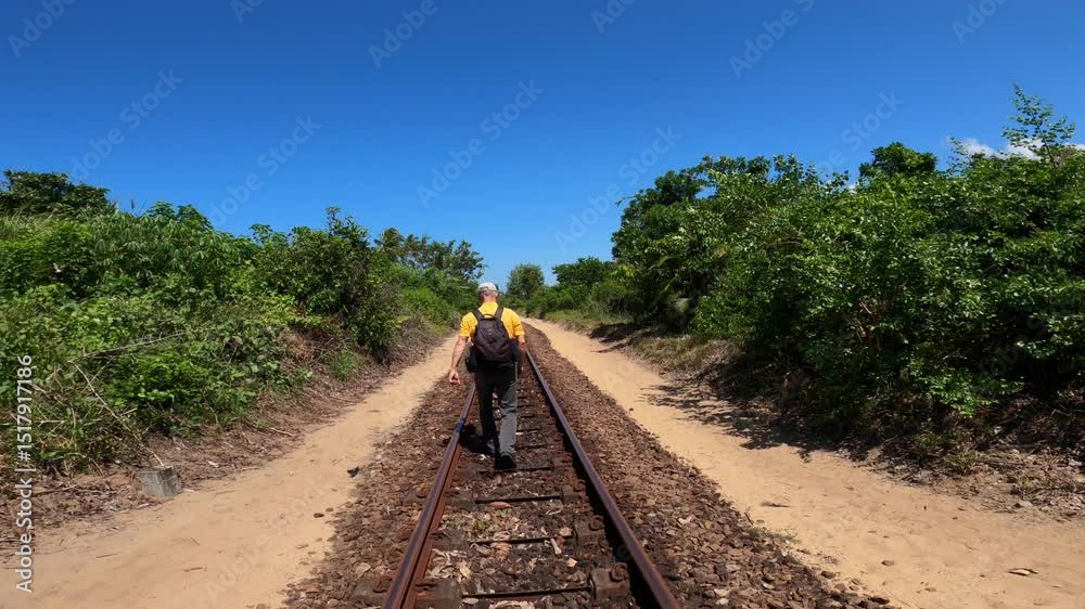 A male tourist walks along a railway track running between the Canal des Pangalanes and the east coast of Madagascar, A man departs from the camera