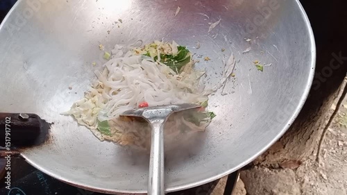 A chef is skillfully frying Kwetiau over a blazing hot charcoal stove. The flames dance and flicker, casting a warm glow as they heat the heavy wok.