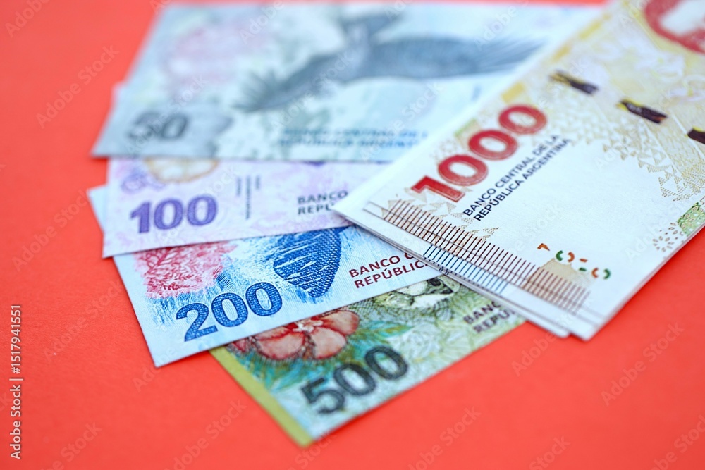 Argentine pesos money bills in big amount lies on red color table close up Argentine pesos money bills in big amount lies on red color table close up