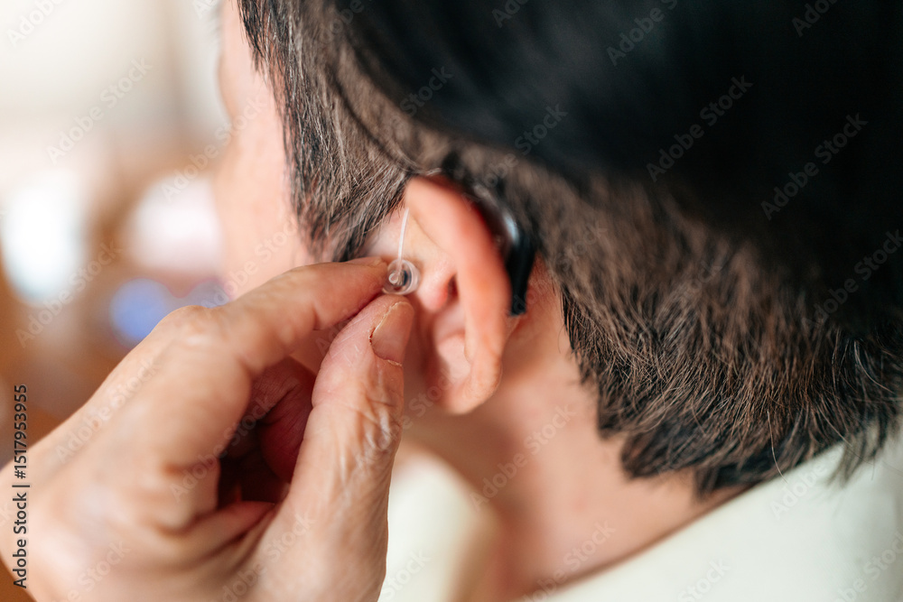 Naklejka premium Senior woman inserting a modern hearing aid behind her ear, showcasing assistive hearing technology for elderly care, independence, and quality of life in a close-up personal moment.