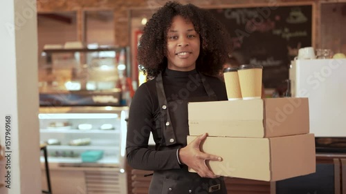 Smiling African American waitress holding cardboard boxes and coffee cups in cafe