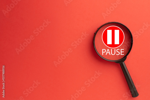 Magnifying glass focusing on a red pause button icon with white bars and 'PAUSE' text.Concept of taking a break,stopping for reflection, work hiatus,analyzing an interruption,or media player control.