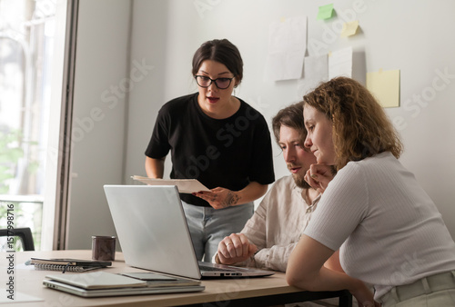 Three software developers brainstorming in a modern office. Team coding session with laptops showing code, planning web development and design. Tech startup environment and teamwork