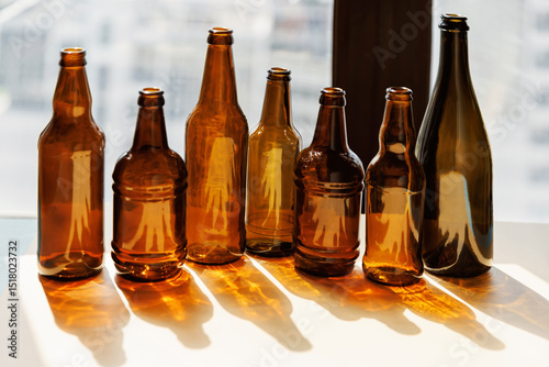 Multiple amber glass bottles arranged on a table in front of a window with shadows and sunlight
