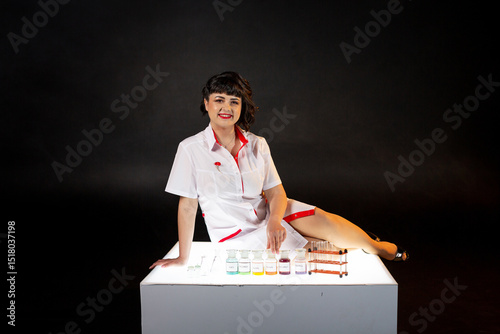 Teacher in a lab coat on a black background with a set of chemical compounds and various glass test tubes photo