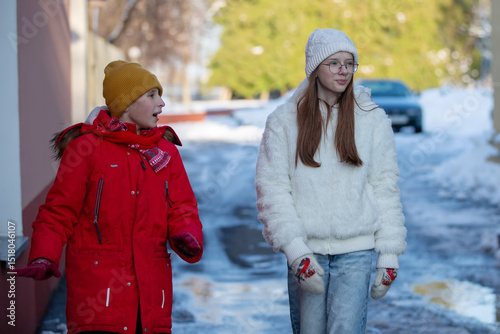 A boy and a girl are walking along a winter city street.