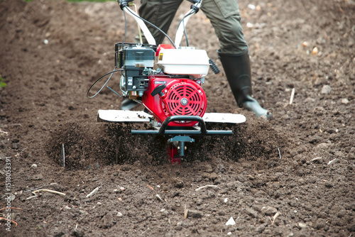 Fotografie Organic farming man cultivates the ground with a tiller preparing the soil for s