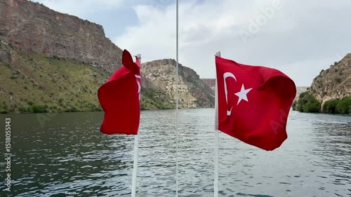 The Turkish National Flag is flying on a Ship Sailing on the Sea. High mountains in the background. The Turkish flag on the bow of the ship. The ship rocks on the waves.