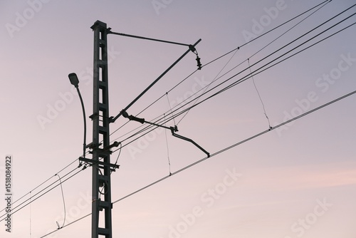Overhead line equipment (OLE) used for railway electrification with catenary system and supporting pole. Infrastructure for trains against pastel evening sky, arrangement of wires and insulators