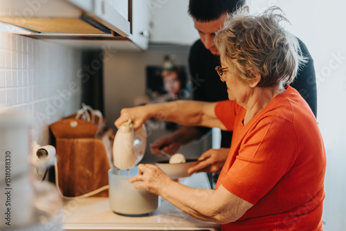 Foto An elderly woman prepares a dough mixture using an electric mixer while being assisted by a family member in a cozy kitchen