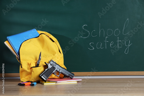 Wallpaper Mural Backpack with gun, knife and stationery on wooden table near blackboard. School safety Torontodigital.ca