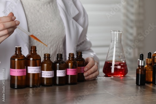 Professional perfumer developing luxury perfume at wooden table in laboratory, closeup