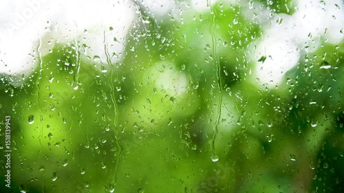 Soothing raindrops streaming down a window with blurred green trees in the background in 4K. Relaxing rainy day view with natural ambient sound. Ideal for mood, nature, or relaxation themes.