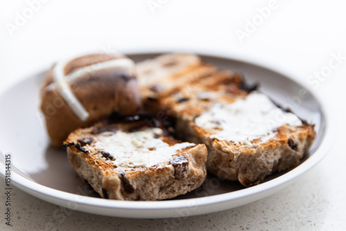 close up of a pair of hot cross buns with butter on them