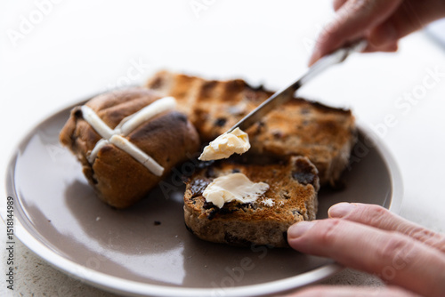 spreading butter onto a toasted hot cross bun