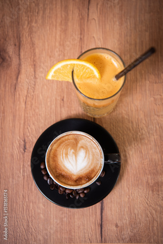 A cozy cappuccino with latte art and a glass of fresh orange juice rest on a wooden table—an inviting, balanced mix of comfort and freshness. photo