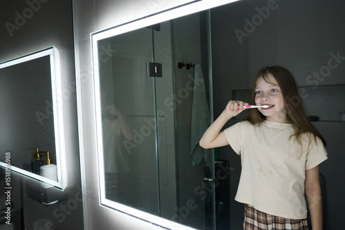 A little girl brushes her teeth before going to bed in front of the bathroom mirror