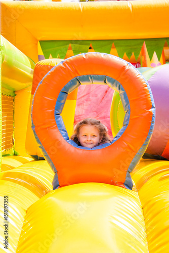 Happy little girl playing on a colorful inflatable bouncy castle. Child in pink outfit jumps with joy. Bright outdoor setting with soft light and vivid colors.

