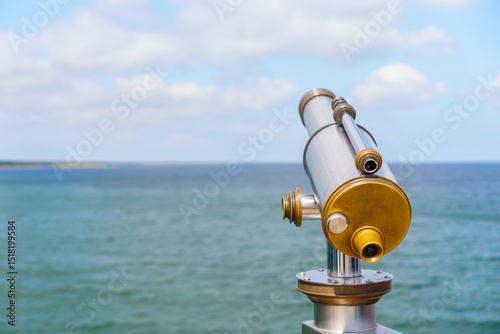 Public telescope on the coast provides a clear view of the ocean under a partly cloudy sky allowing for travel planning and observing the horizon from the viewpoint