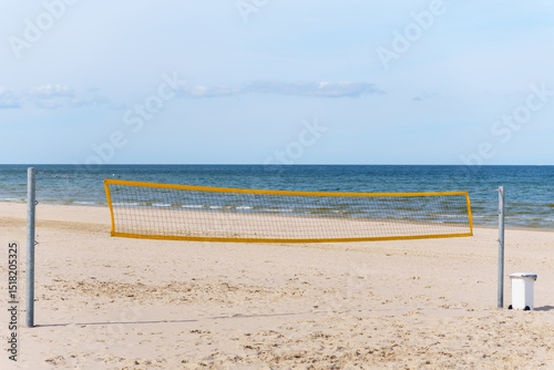 Fototapeta Naklejka Na Ścianę i Meble -  Beautiful summer day on an empty beach with golden sand shows a volleyball net ready for a game with the blue ocean and sky offering a scenic sports beach vacation scene