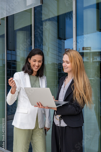 Business meeting outdoors with two professional women in their 30s of different ethnicities discussing ideas using a laptop in an urban setting