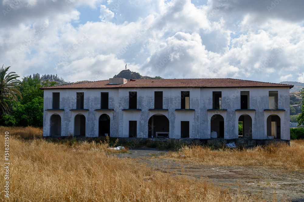 Fototapeta premium An unfinished residential building stands against a mountainous backdrop featuring the iconic Ataturk silhouette, a symbol seen across Northern Cyprus.