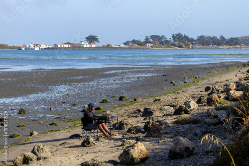 A man with a laptop working on a beach or bay at low tide.  Full-time RV nomad lifestyle, working in shorts from his home office.