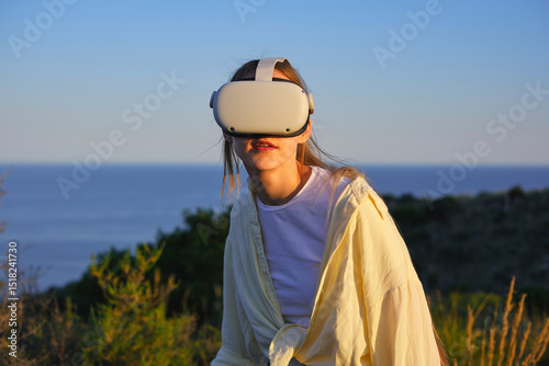 Woman immersed in virtual reality with headset outdoors at sunset