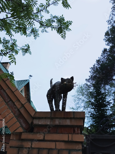 Metal statue figurine cat on the brick wall of the house. Summer twilight.