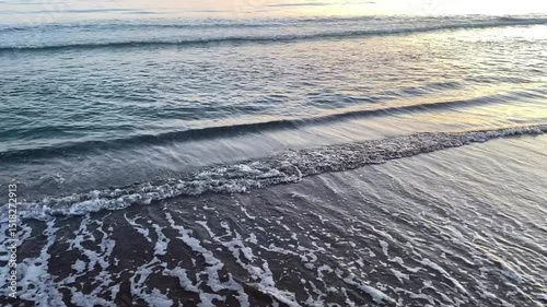 Gentle ocean waves roll in slow motion under a glowing sunset sky.