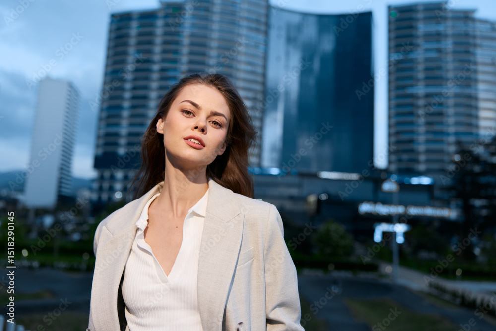 Fototapeta premium confident woman in beige blazer with modern cityscape background during evening light, urban style, business fashion, stylish professional young woman