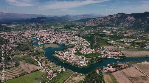 Aerial view of Dalyan River winding through Koycegiz town, surrounded by mountains, agricultural fields, and lush greenery in Mugla, Turkiye