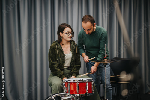 Fotografia A male instructor attentively helps a female student practice drumming skills in a quiet rehearsal studio, emphasizing music education and collaboration to develop their percussion techniques