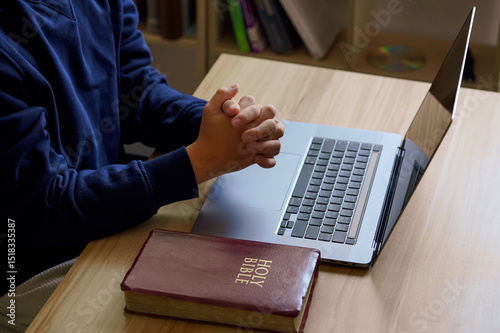 Christian online technology concept. Hands praying of christian with digital computer laptop, Online live church for sunday service. Asian catholic man are reading Holy bible book and online study.