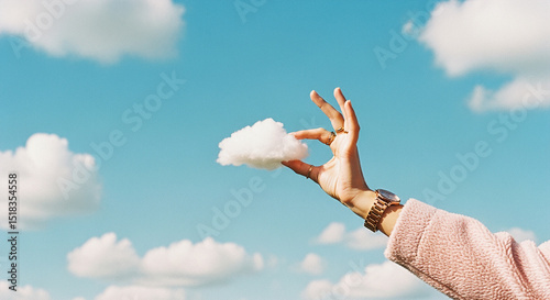 Woman's hand holding a small cloud against a blue sky