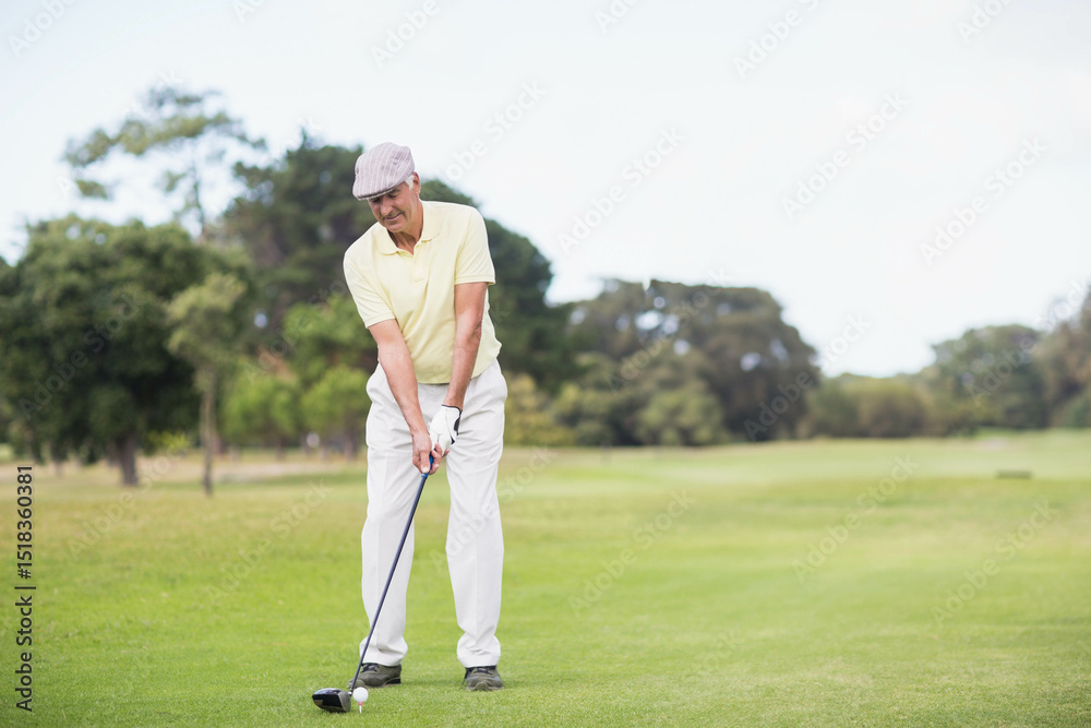 Fototapeta premium Senior man holding driver, wearing golf glove preparing to hit ball off wooden tee on fairway