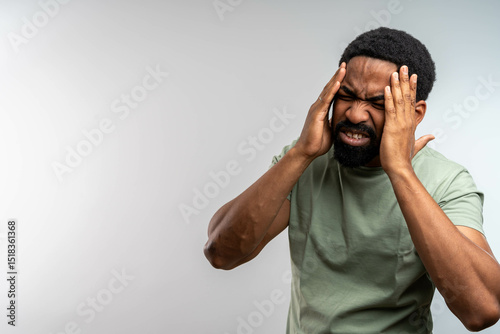 Portrait of young man isolated on gray background, suffering from severe headache, pressing fingers to temples with closed eyes