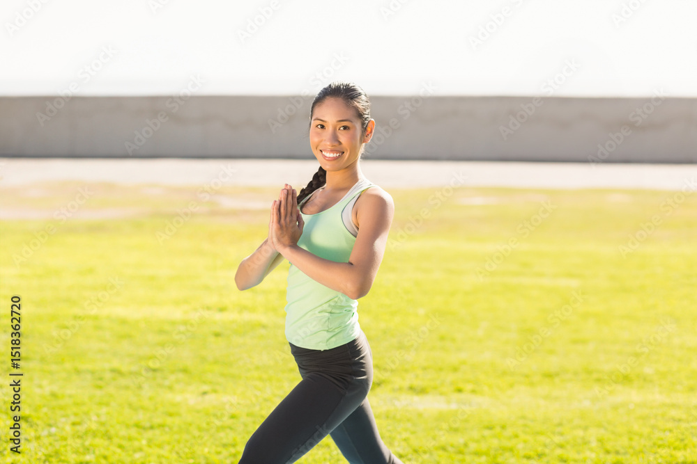 Asian woman standing on grassy lawn holding prayer pose against concrete wall under bright sunlight Asian woman standing on grassy lawn holding prayer pose against concrete wall under bright sunlight