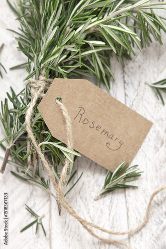 Fresh green rosemary sprigs with kraft paper text label on white weathered wooden table top view
