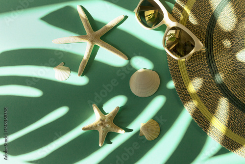 Creative summer composition with trendy sunglasses, hat, starfishes and shells on background with monstera leaf shadow. Vacation concept