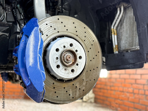 Car ventilated front brake disc with blue caliper. Modern perforated brake disc with ventilation holes, cooling. The process of washing radiators, intercoolers and car suspension. Car wash close up. 